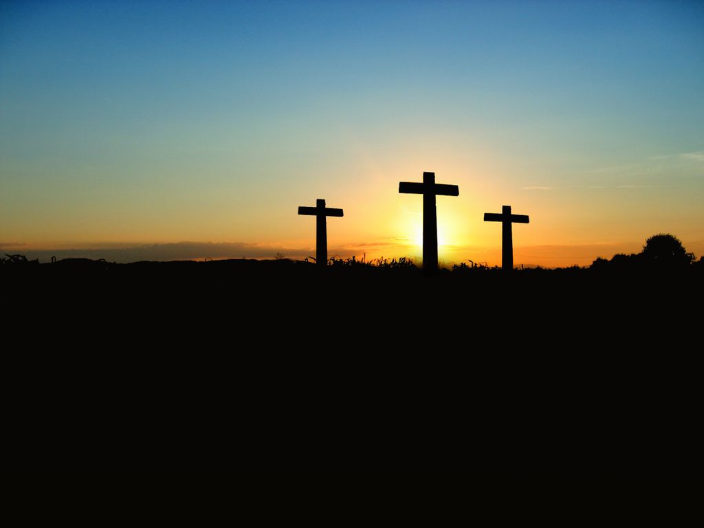 Silhouette of three crosses against a vibrant sunset sky.